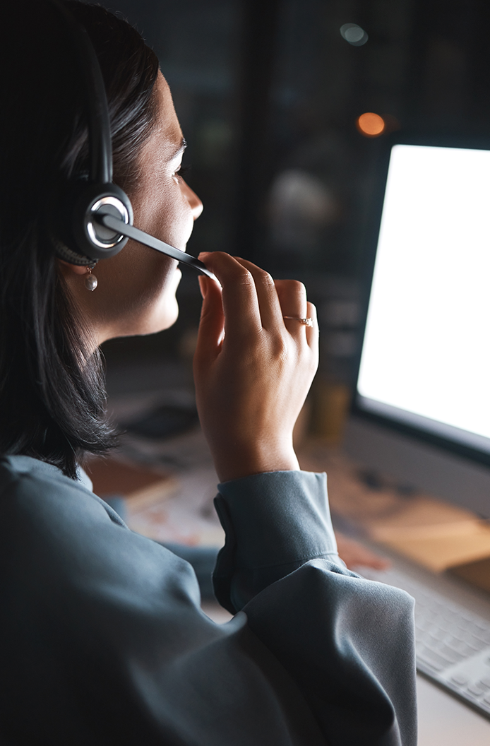 A woman speaks into a headset and looks at a computer as she works at a customer service call center